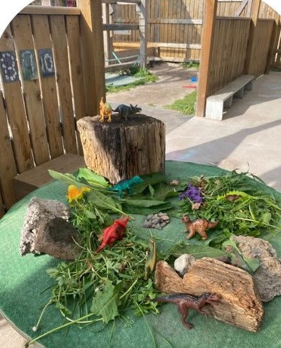 Dinosaur small world built from leaves, logs and stones on the outdoor table