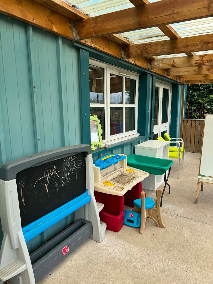 The covered outdoor play area under the pergola — a chalkboard, mud kitchen and water-play tables